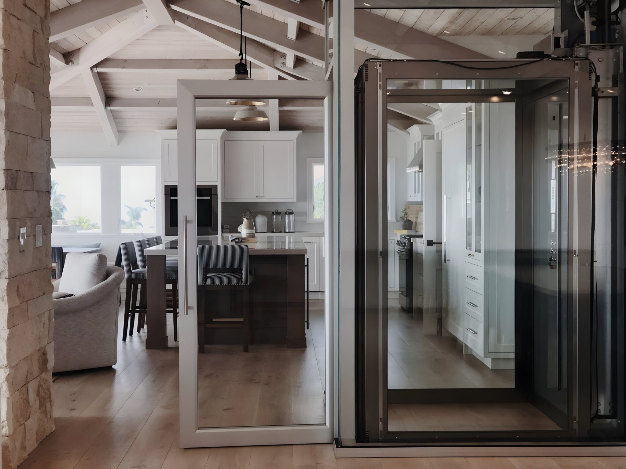 Glass-shaft E1 Swing Door lift beside a stone feature wall in the open-plan kitchen and living area of a Laguna Beach home