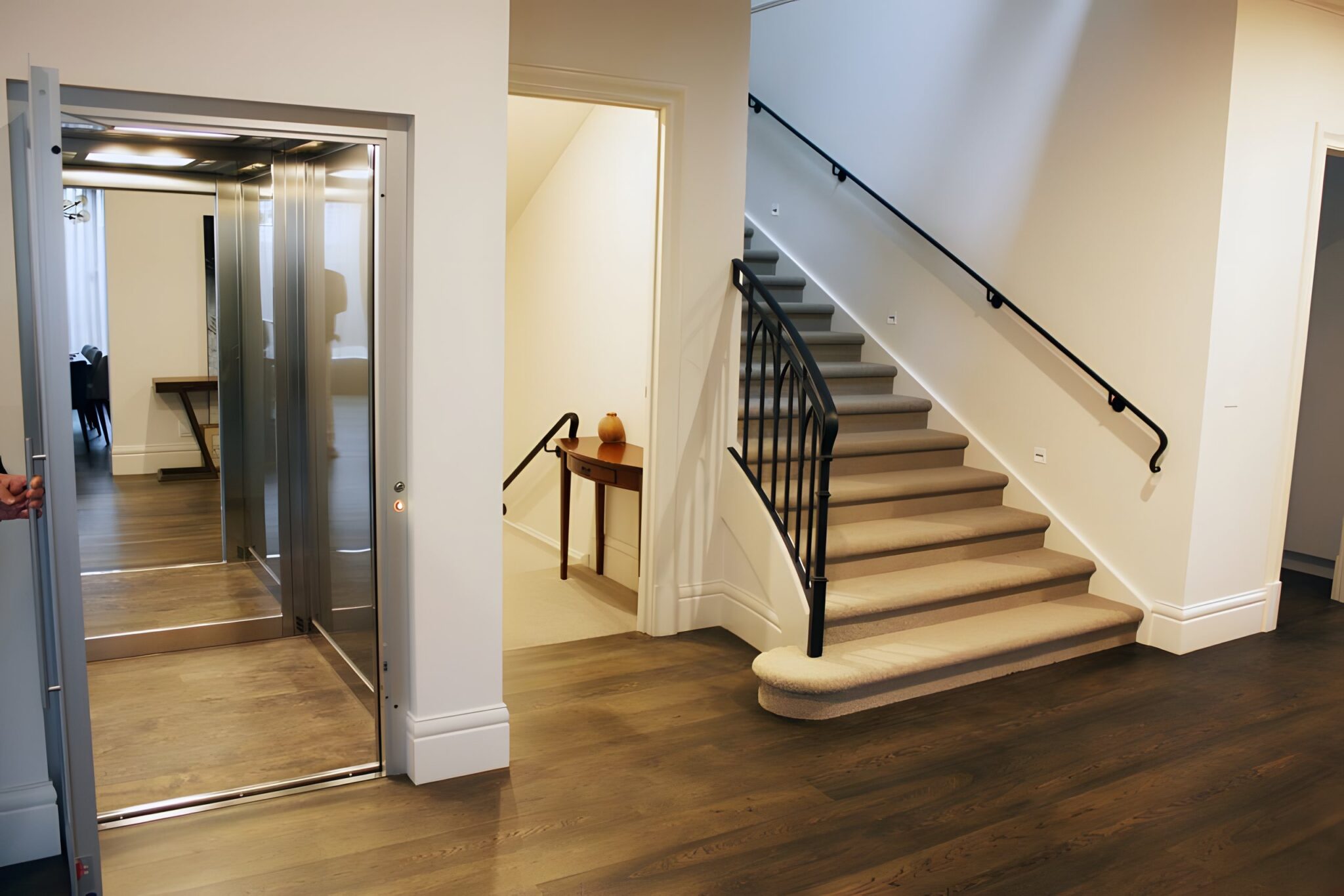 Open lift door with a dark timber floor beside a staircase and black handrail