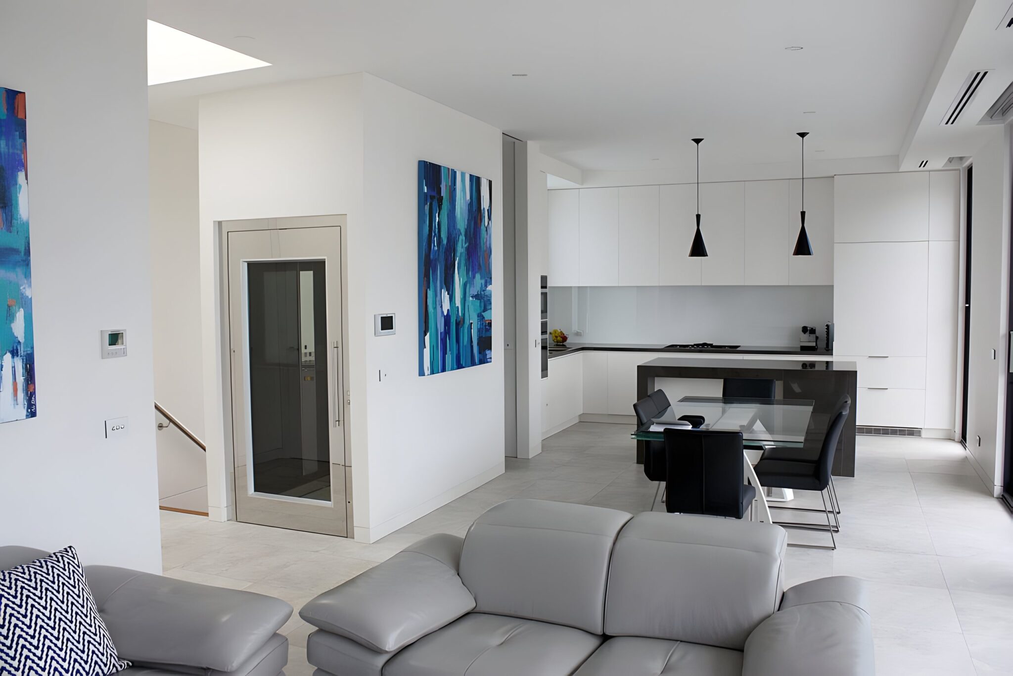 Open-plan living and kitchen area in a Brighton home with a stainless steel and glass lift door beside a blue painting