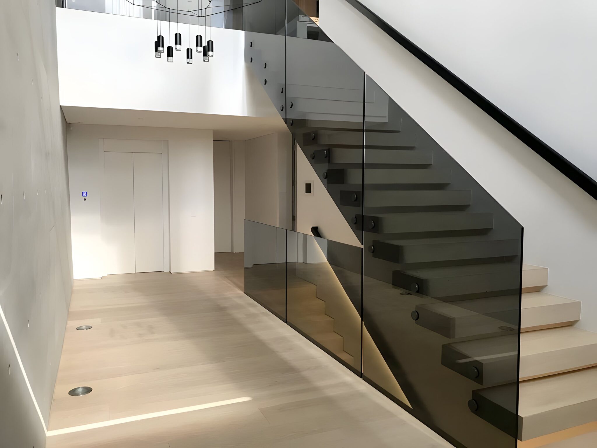 Concrete walled entry hall with a floating staircase and glass balustrade, and the lift door beyond, in a Maroubra home