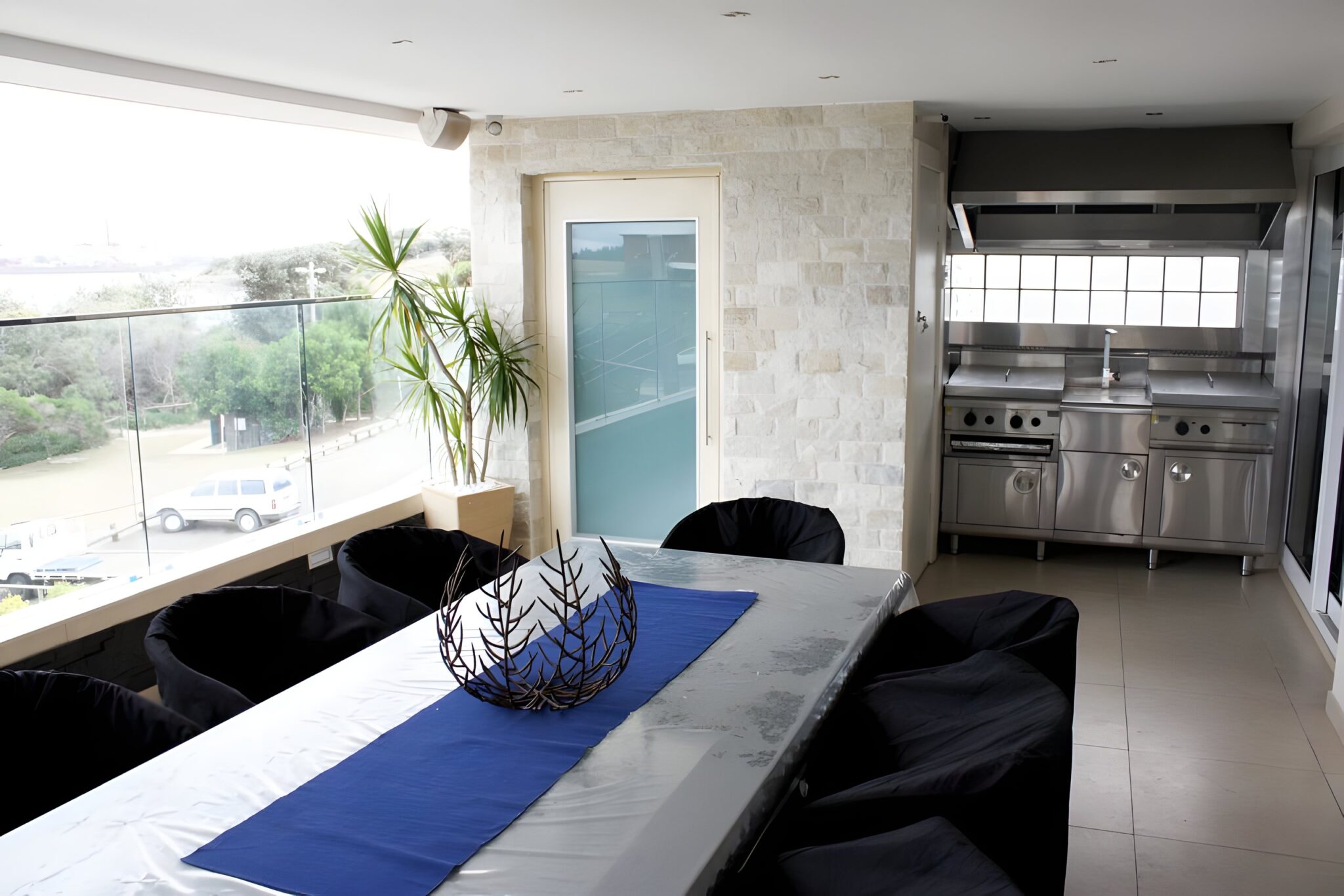 Frosted glass lift door set in a stone-clad wall beside a dining table and a balcony overlooking the bay