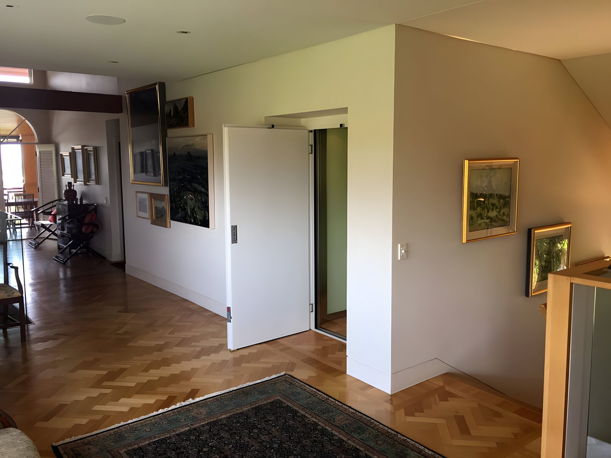 Parquet floored hallway in an Auchenflower home with a flush white lift door beside framed artworks