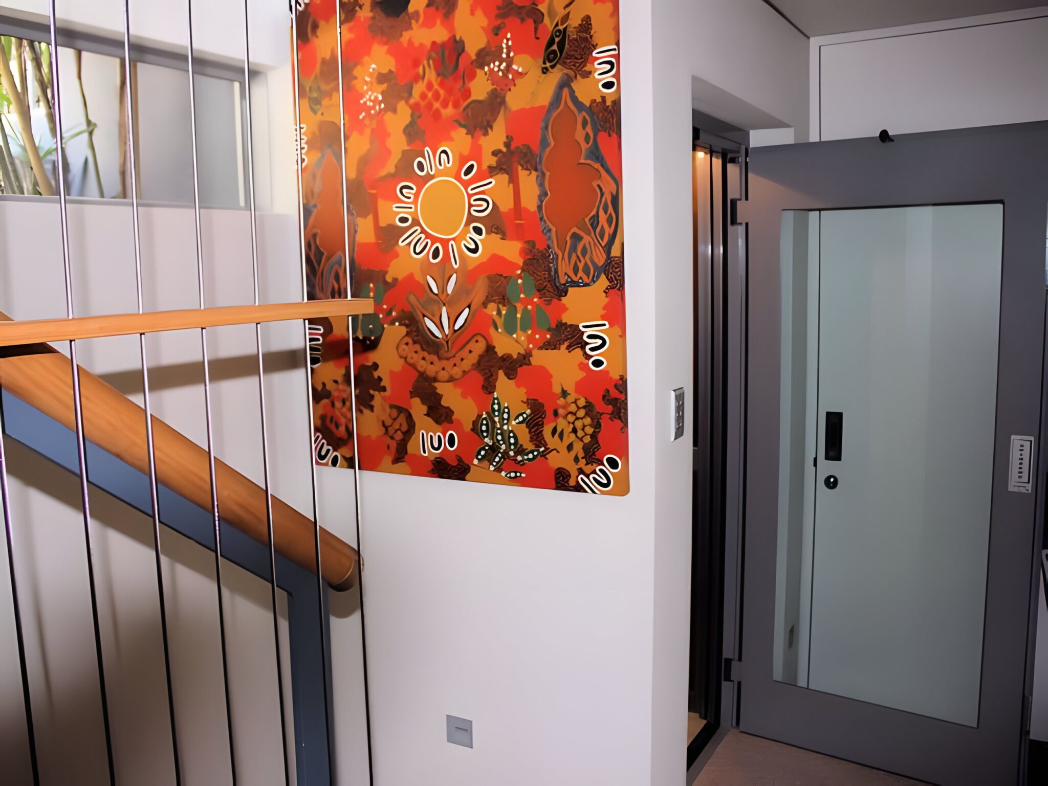 Frosted glass lift door beside a colourful artwork and a timber-handrailed stair in a New Farm home, Brisbane