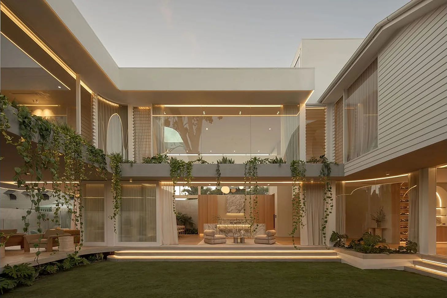 Two-storey family home wrapped around a lit courtyard at dusk in New Farm