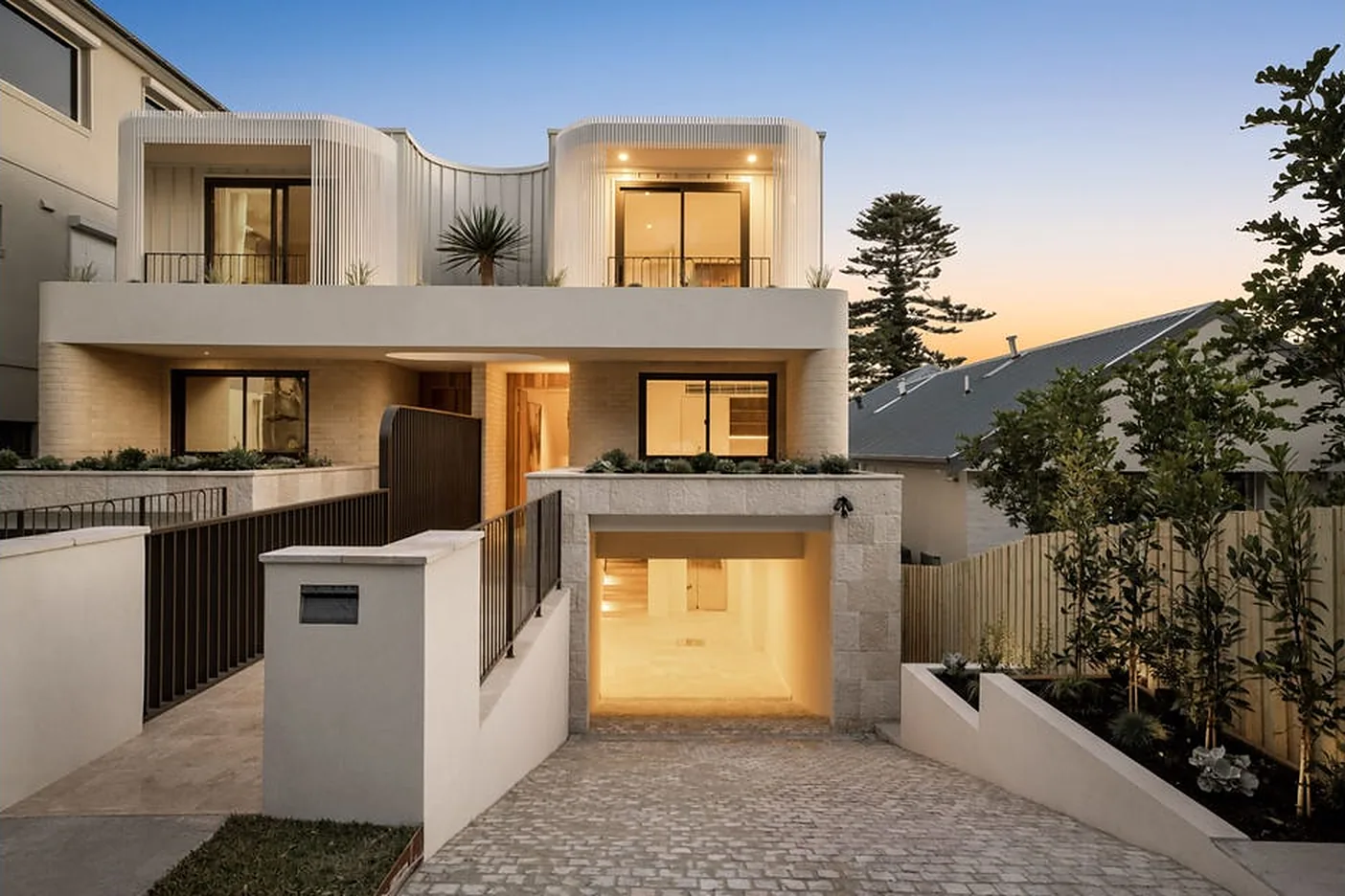 Stone and render North Bondi home at dusk with a lit garage
