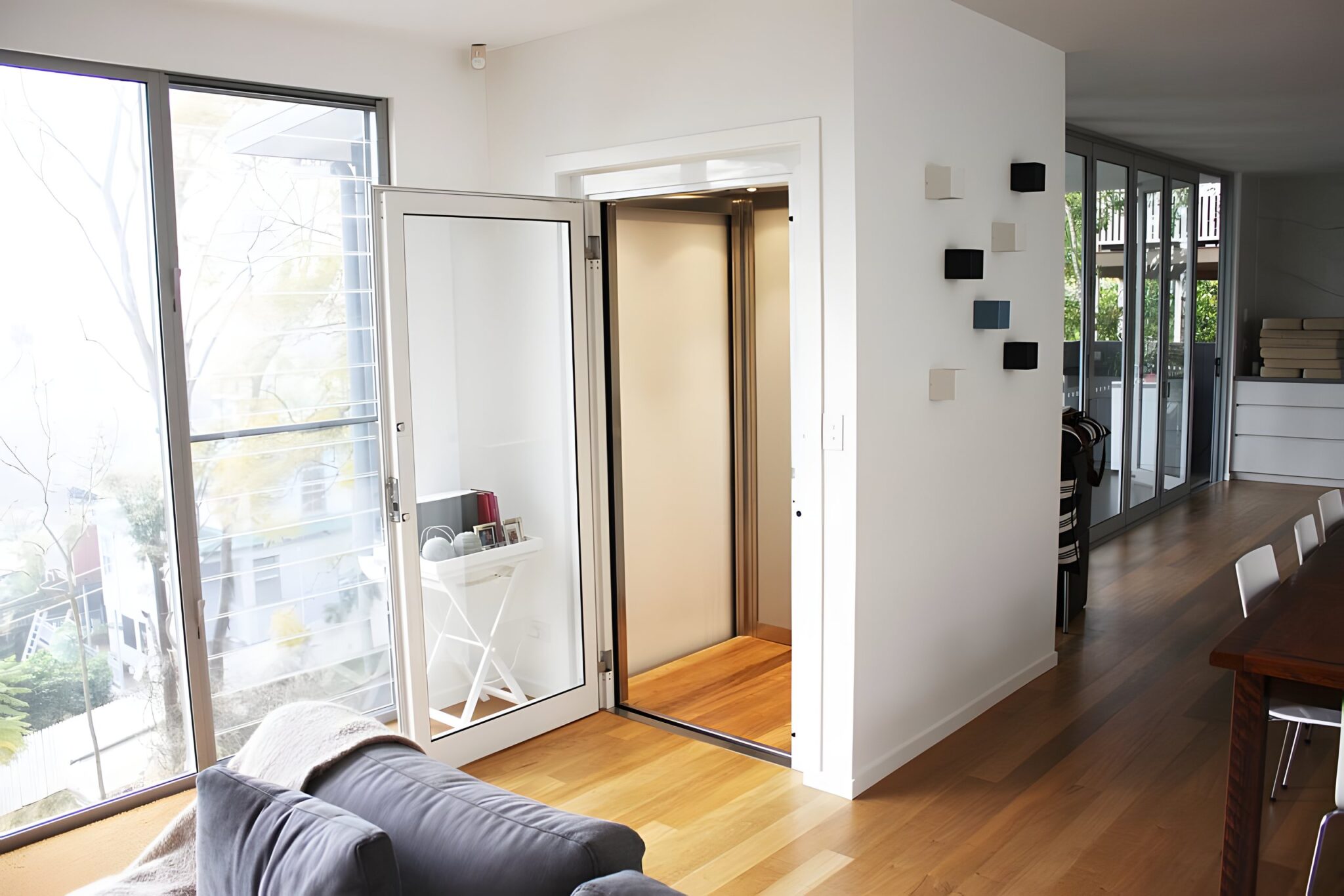 Living room with the glass landing door of the home lift open beside a full-height window