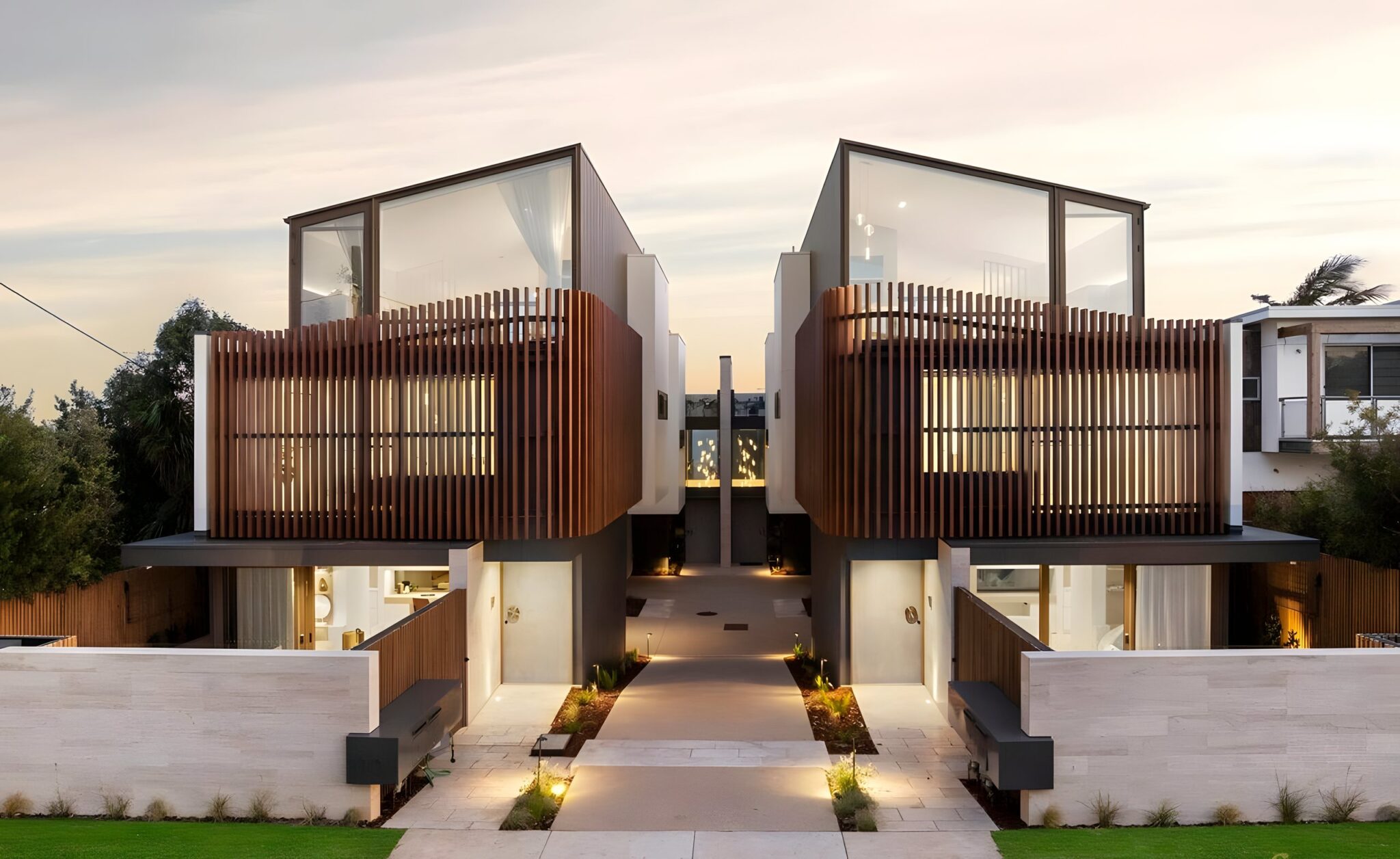 Two three-level coastal townhouses in Ocean Grove with timber screening, lit at dusk