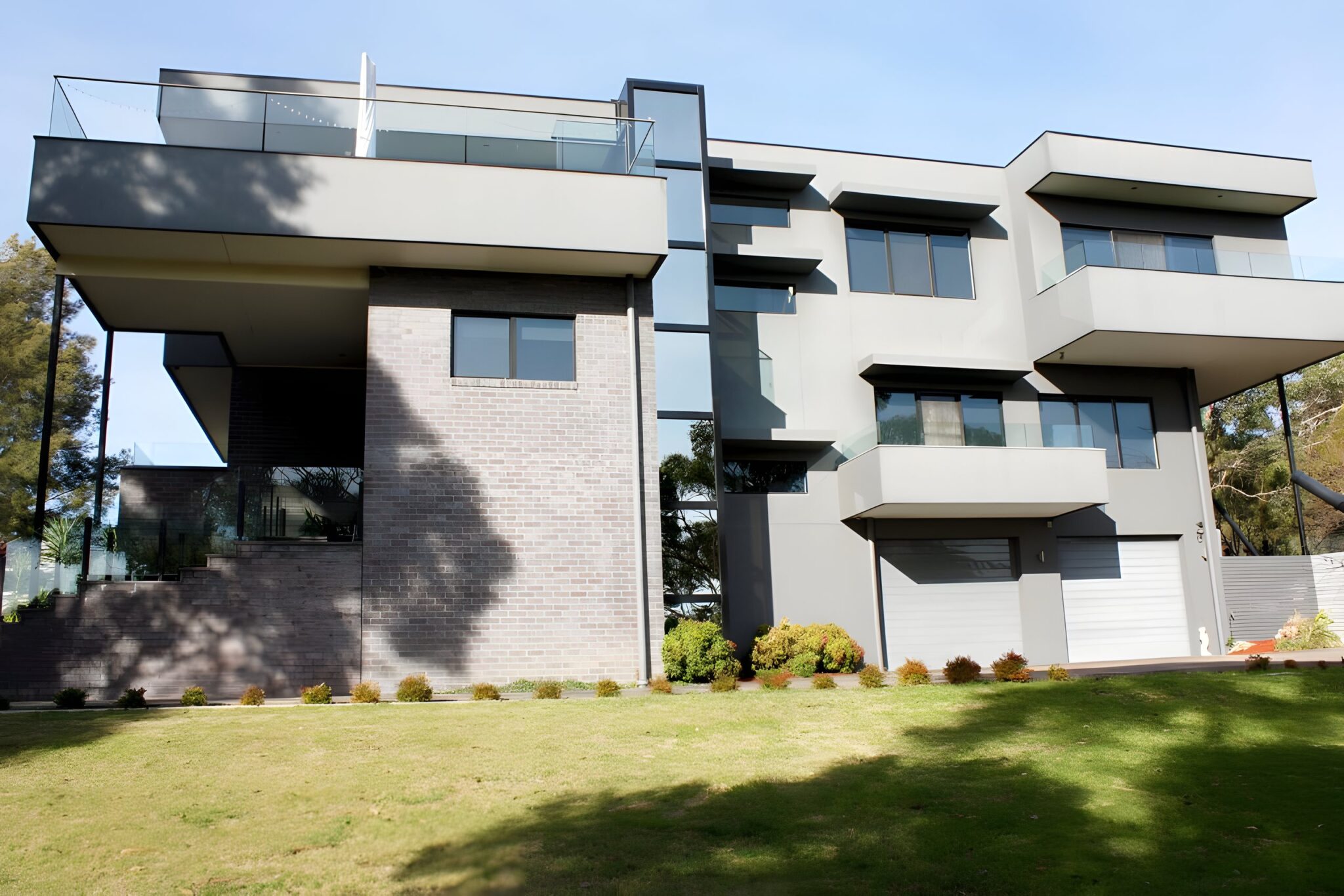 Three-storey house with a black framed glass lift tower set between two building forms, seen from the lawn