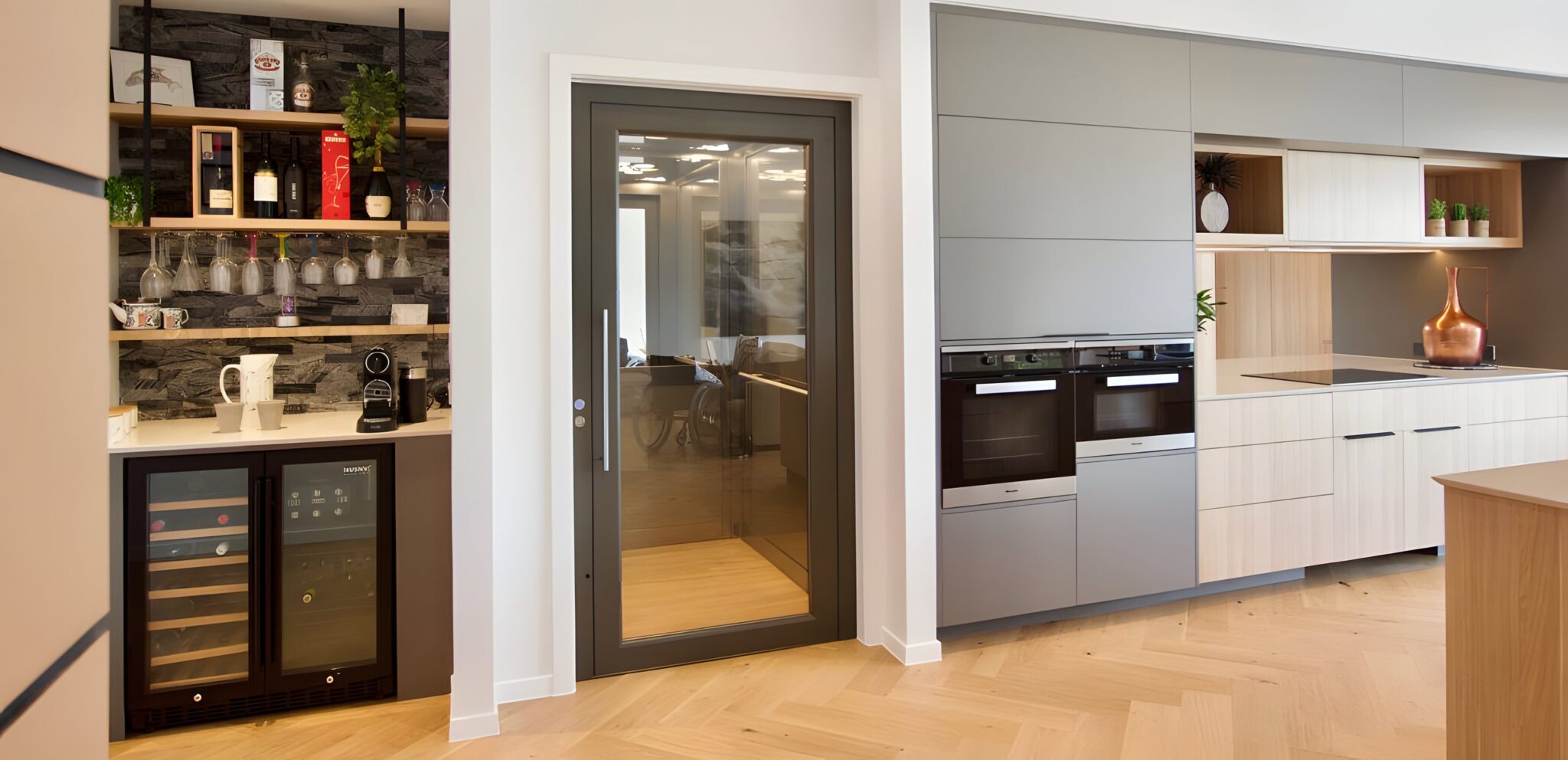 Glass-panelled lift door in the open kitchen of the Pavilion Home, beside a wine fridge and wall oven