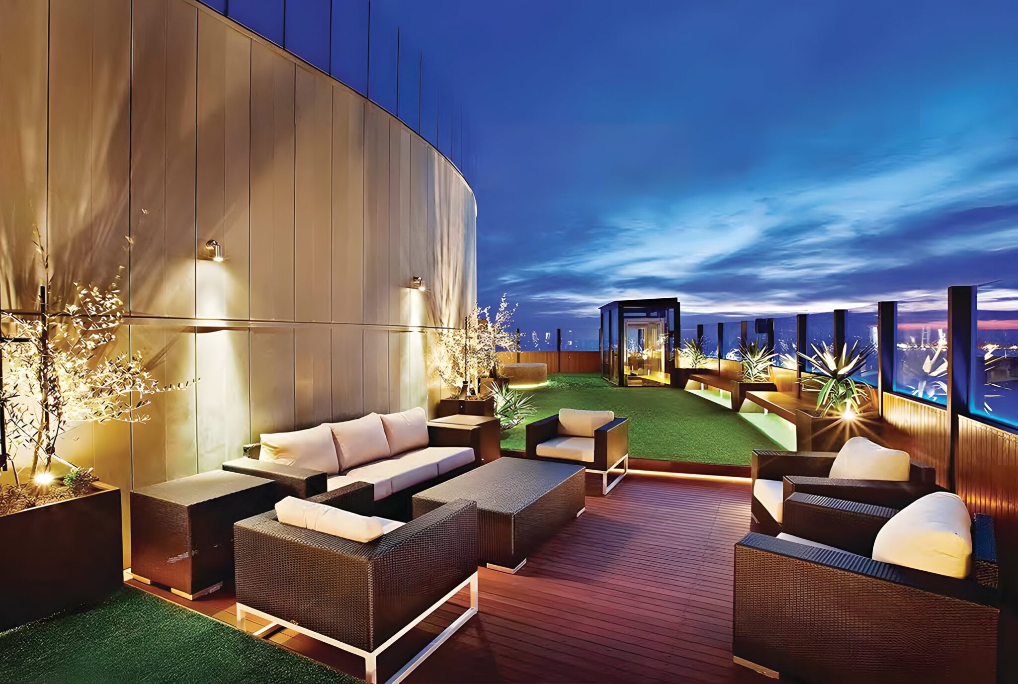 Penthouse rooftop terrace in Melbourne with outdoor lounge furniture, lawn and a glass lift enclosure under a dusk sky