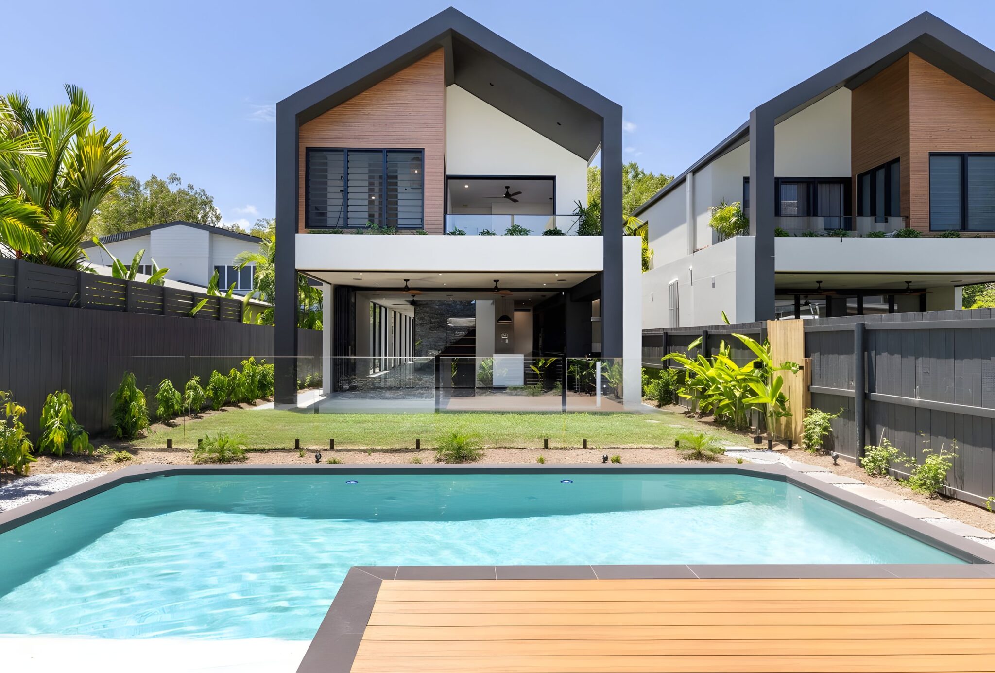 Two-storey gabled Port Douglas villa with timber cladding and black frames, seen across its pool and deck