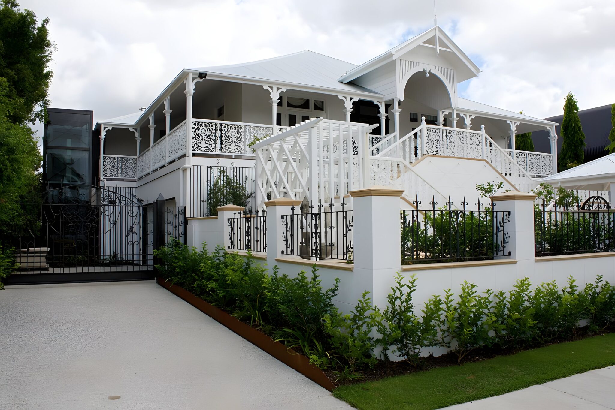 Restored white Queenslander home with fretwork verandahs and a black glass lift shaft at the left of the house