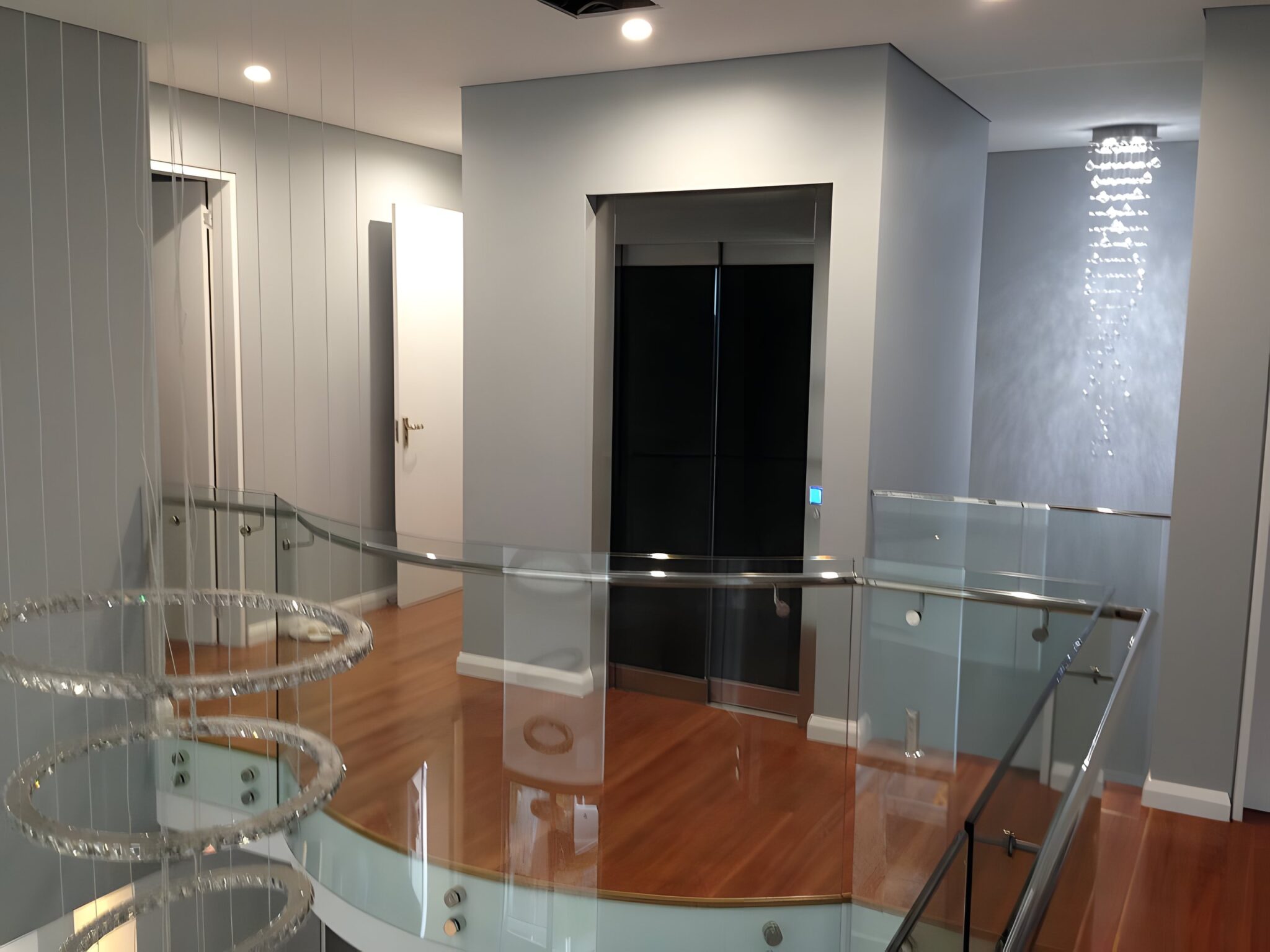 Landing with a crystal chandelier, glass balustrade and the lift door beyond in a Randwick home