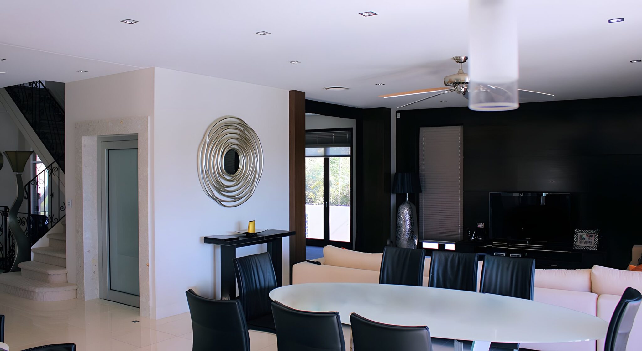 Open-plan dining and lounge in a Sanctuary Cove home with a glass-door lift set in a stone surround beside the stairs