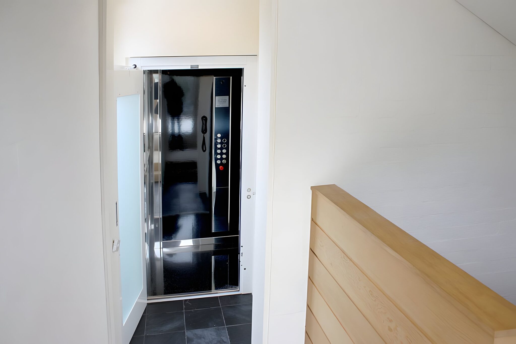 Lift door with a push-button panel at the top of a timber stair rail in the retrofitted six-level home