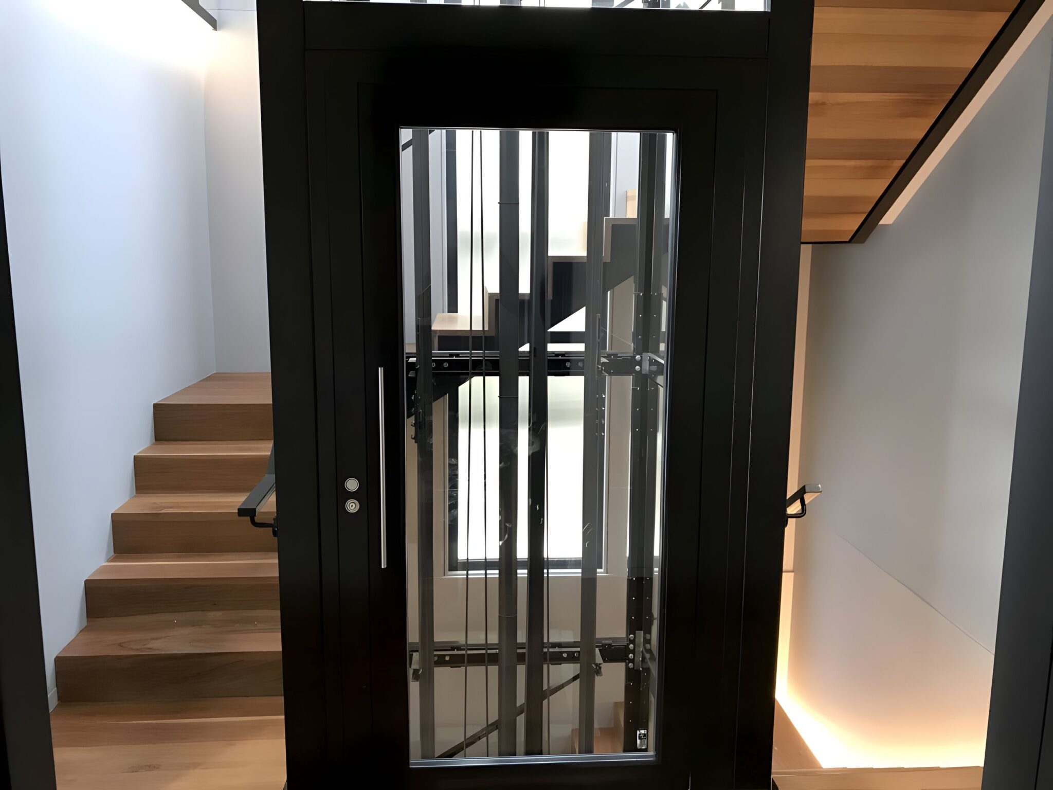 Black framed glass lift beside a timber staircase with lit steps in a Balmoral home, Sydney