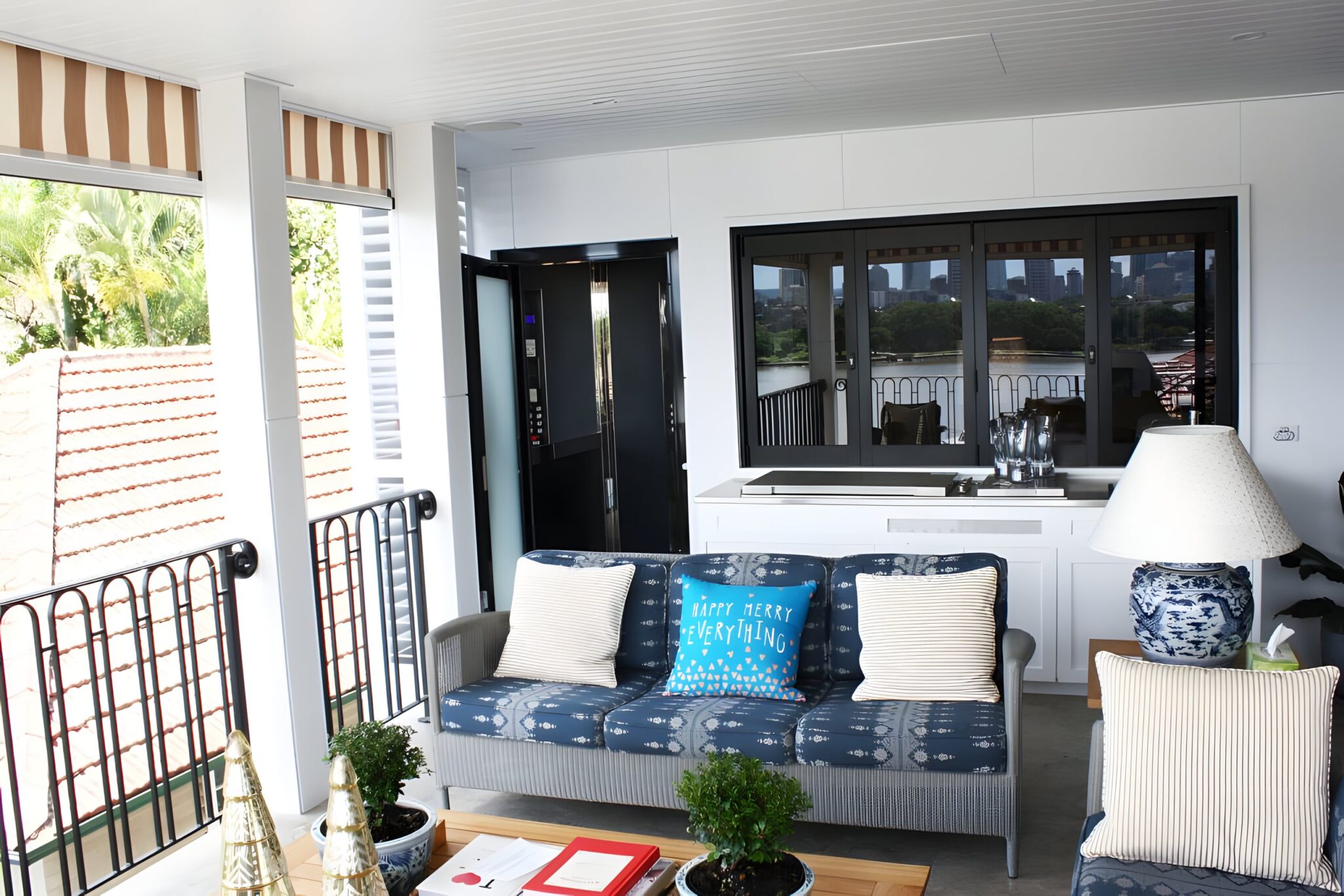 Black framed lift door open on a Newmarket balcony beside a blue patterned sofa, with the Brisbane river and city beyond