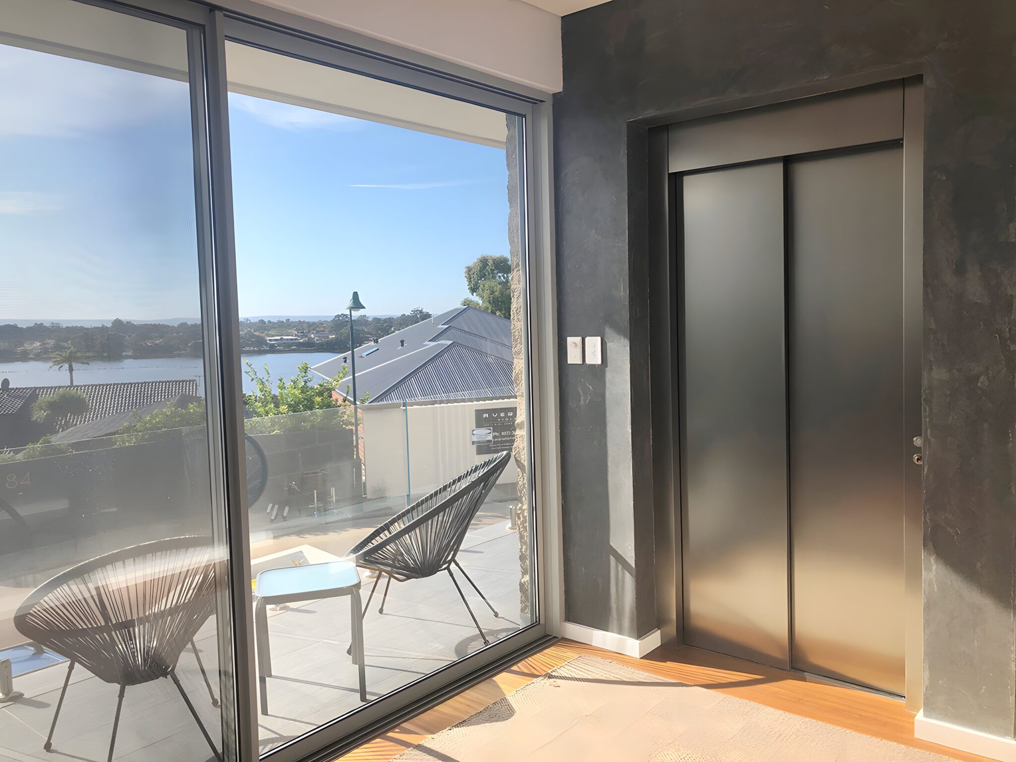Stainless steel lift doors set in a dark feature wall beside a sliding glass door with river views, Salter Point