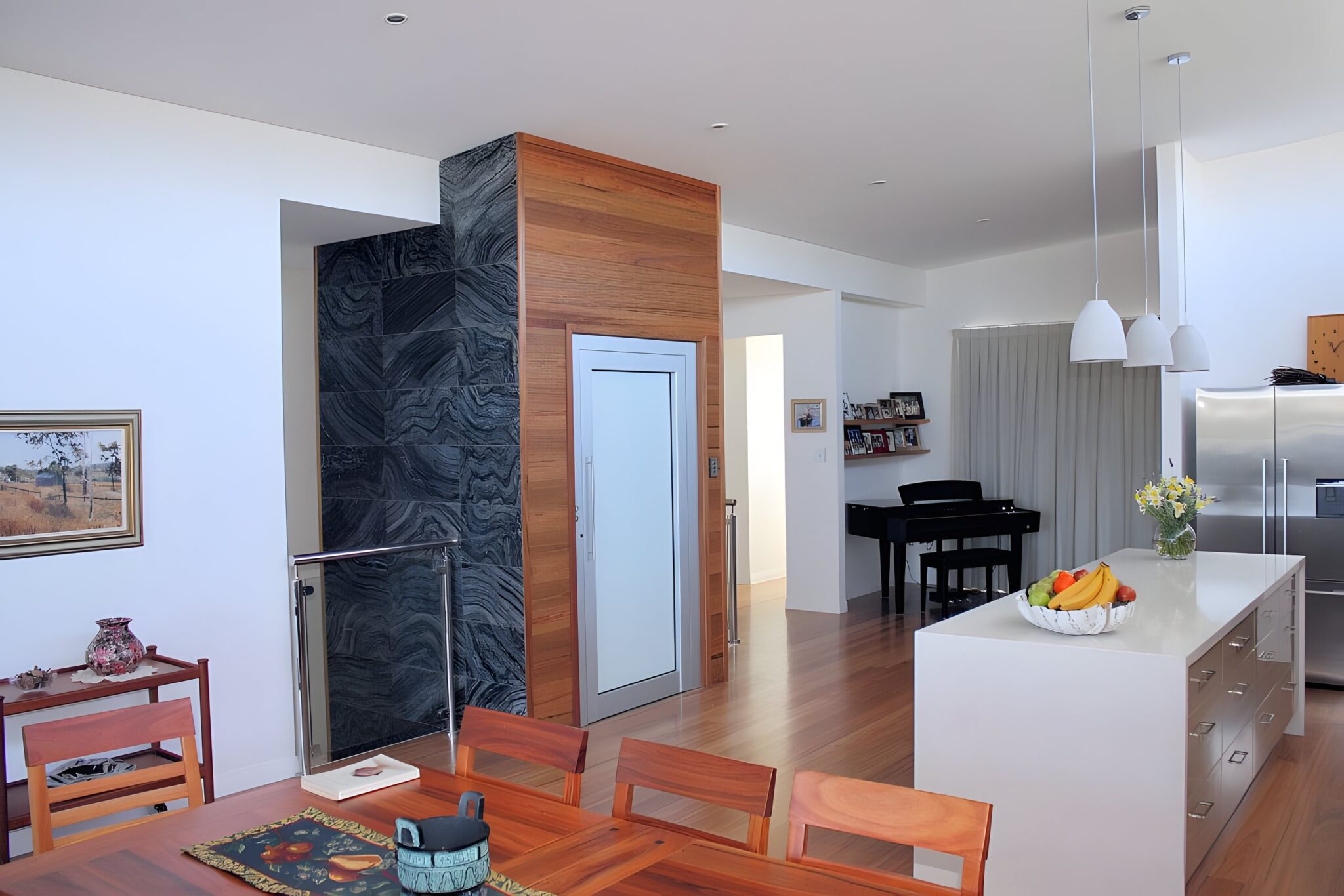 Open plan living area with a black marble and timber clad lift shaft beside the kitchen and dining table