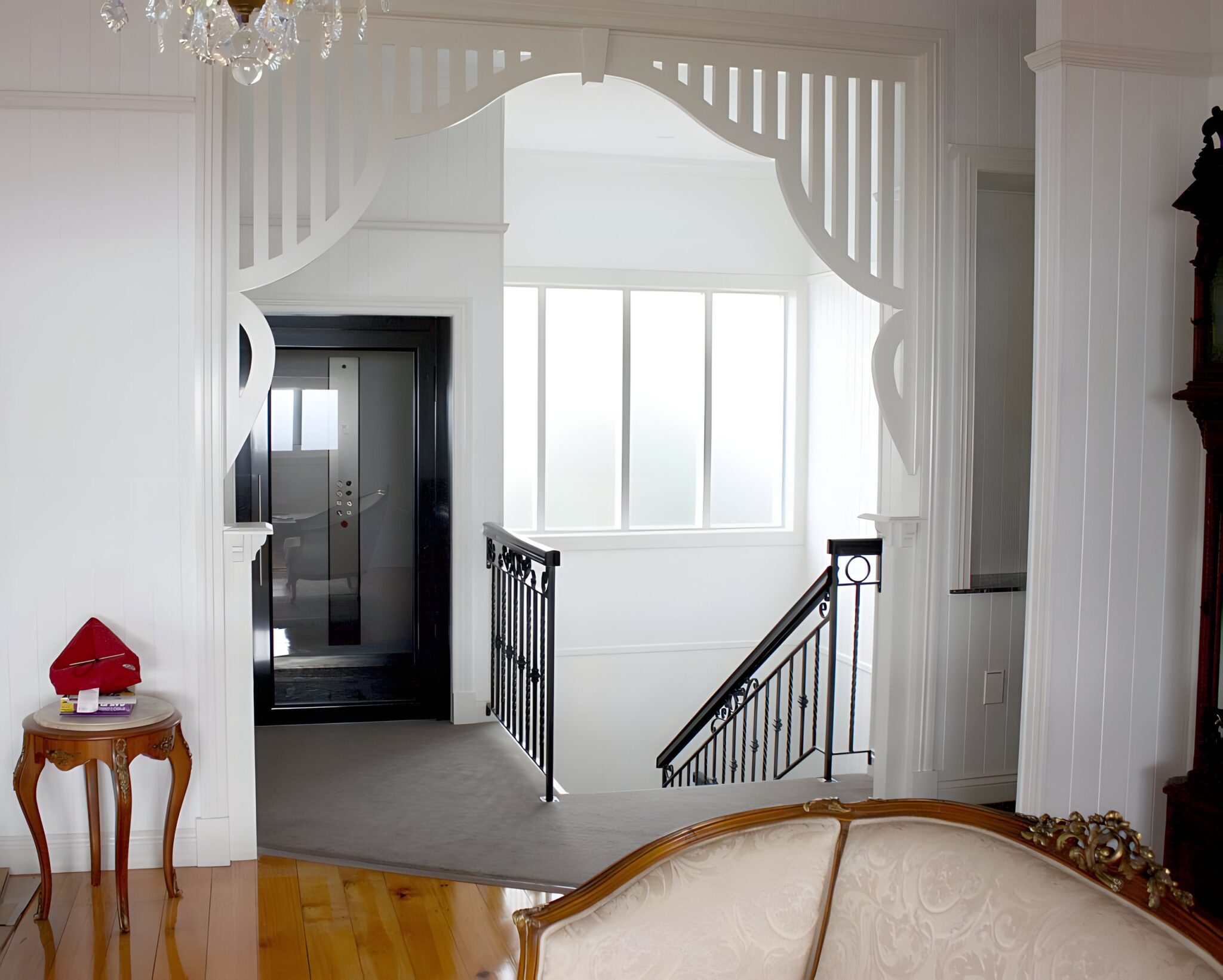 Heritage hallway with a white fretwork arch and black iron balustrade, with the black-doored lift beyond