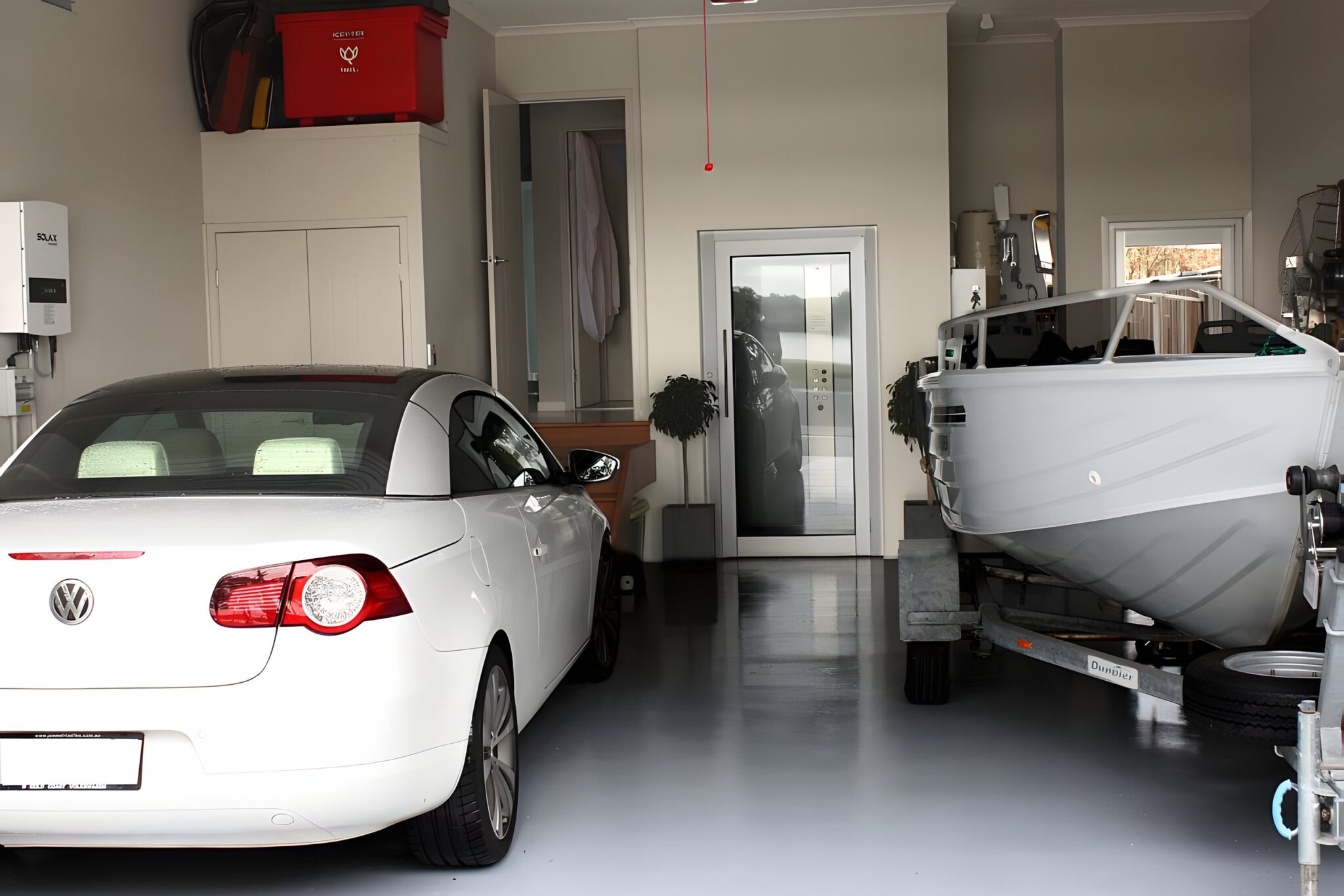 Garage with a white convertible and a boat on a trailer, with the glass door of the home lift beyond