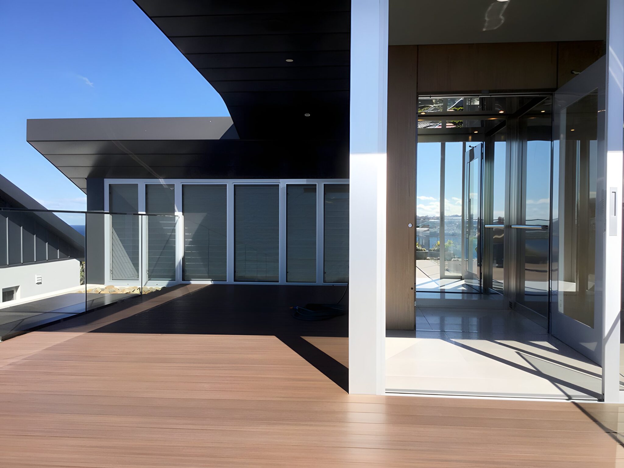 Lift doors opening onto a timber deck with sea views at the South Coogee development