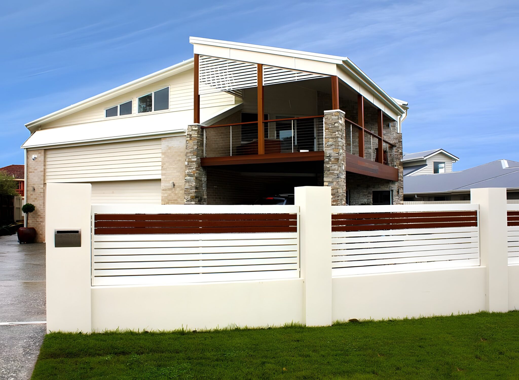 Two storey home with a timber balcony, stone cladding and a white front fence under a blue sky