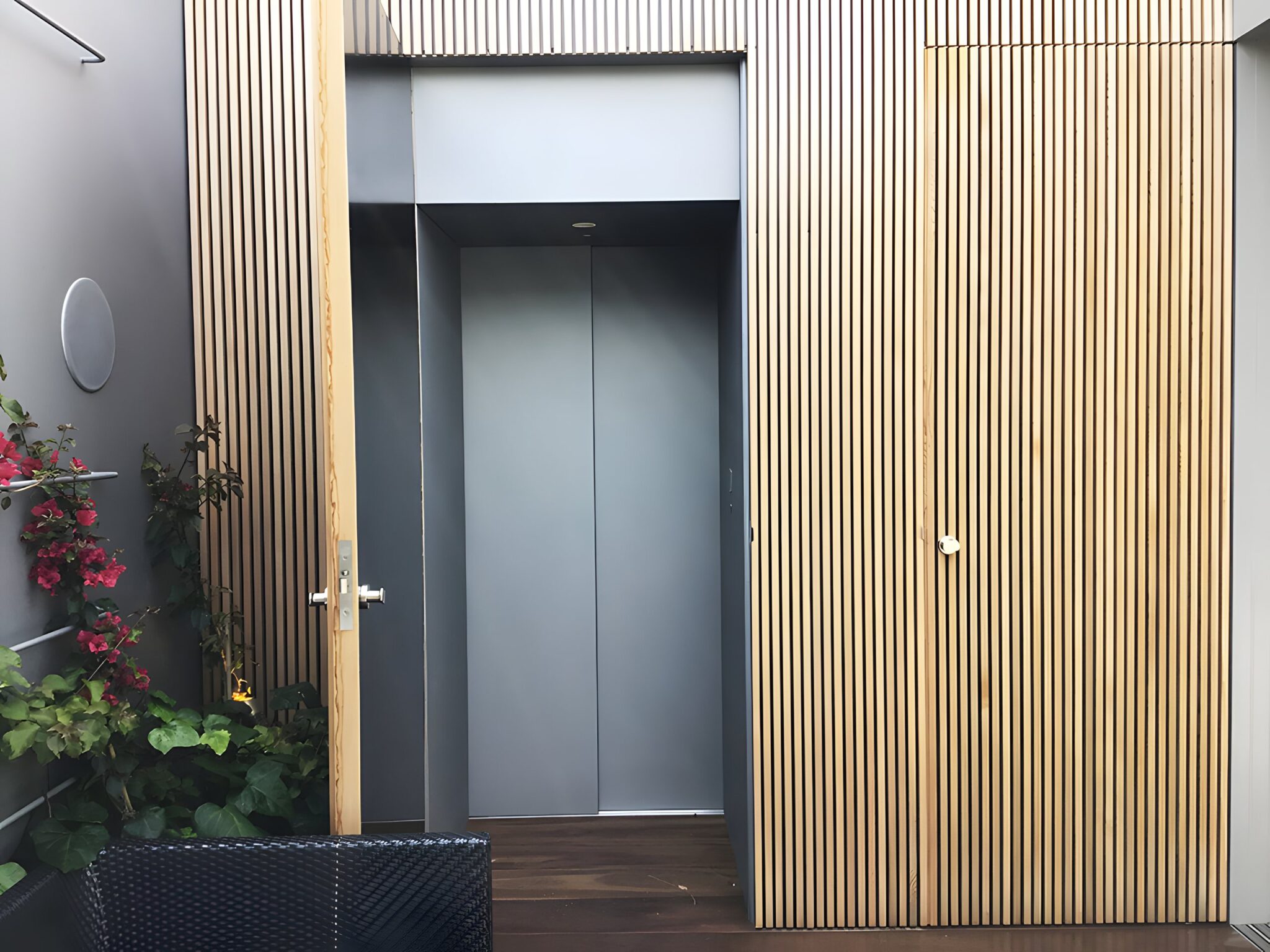 Lift door beside timber batten wall panels and a flowering plant at the Vaucluse home
