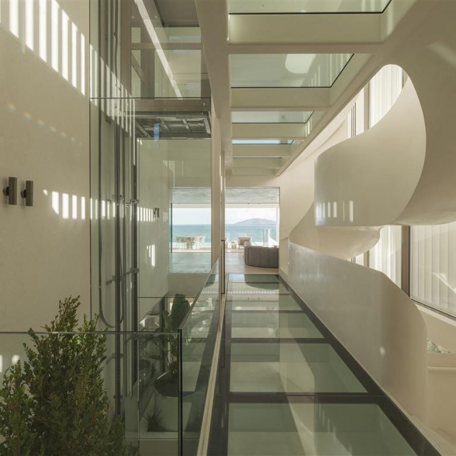 Glass-floored walkway beside a glass Lift Shop home lift shaft and white spiral stair, ocean view